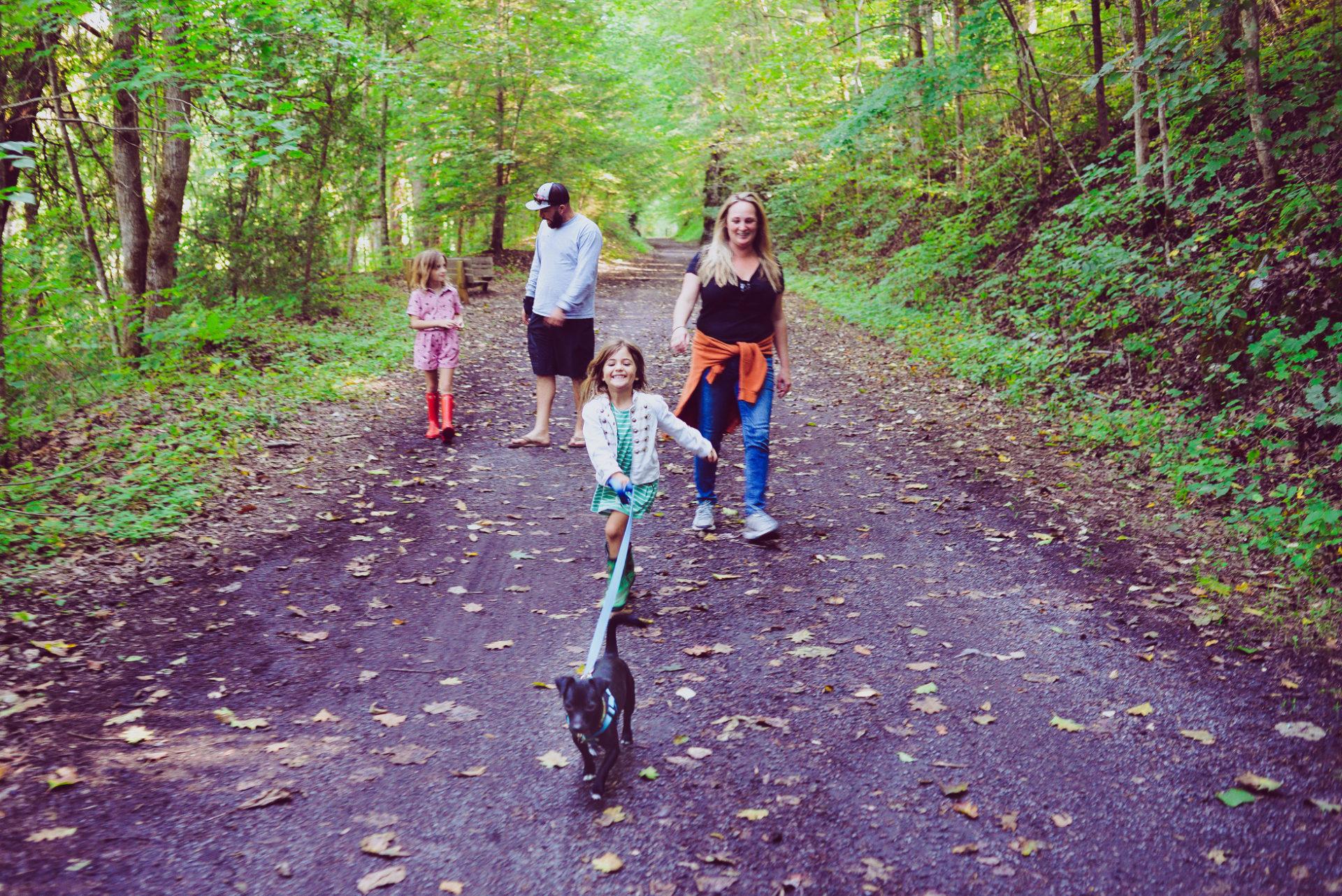 parents and two children with dog hike down a road in the forest